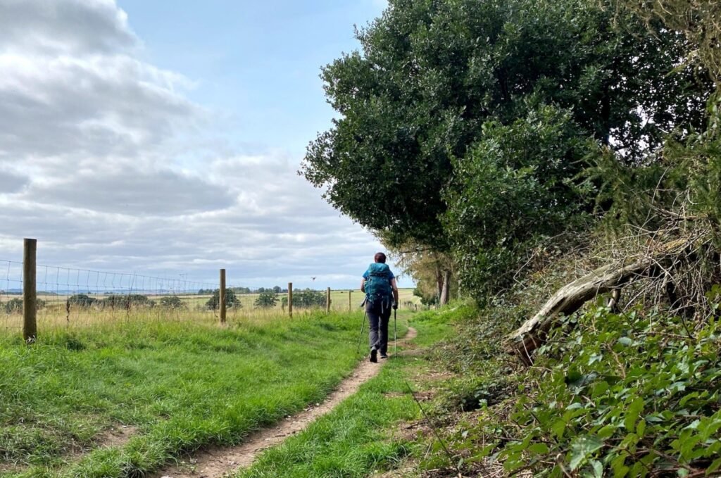 Distant person walking along a quiet rural path under open sky.