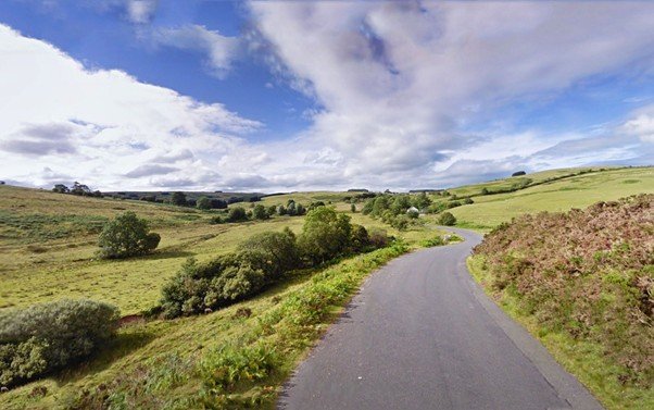 Straight rural road stretching through open countryside under a calm sky.