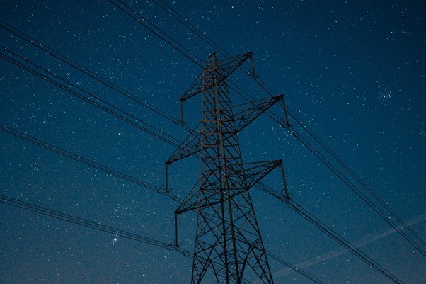 High voltage transmission tower under dark storm clouds.