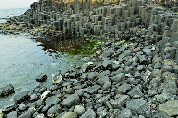 Tall hexagonal basalt rock columns forming a vertical cliff face.