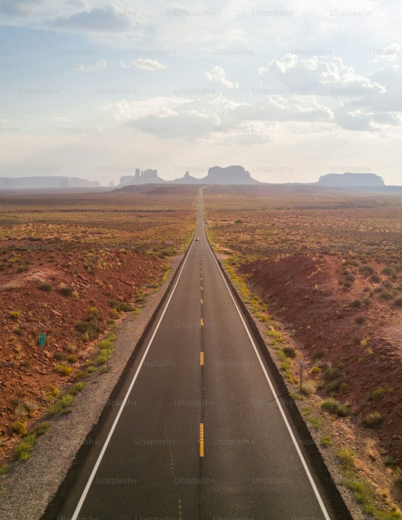 Straight two-lane road crossing arid landscape toward distant horizon.