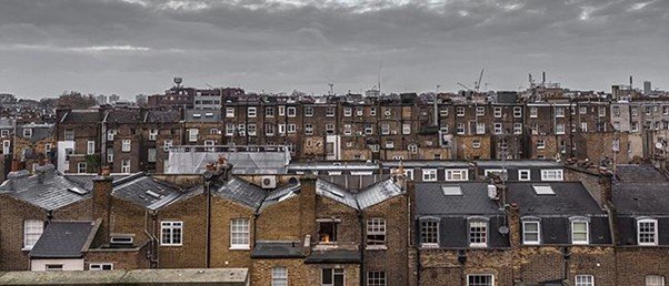 Rows of brick rooftops and chimney pots under grey sky.