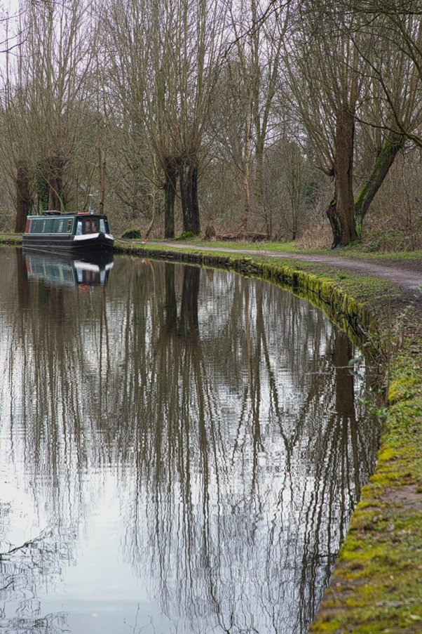 Canal towpath running alongside still water with trees along the bank.