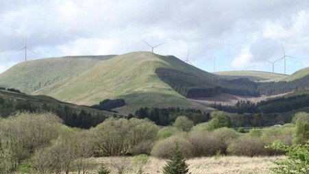 Wind turbines standing across a grassy ridge in open countryside.