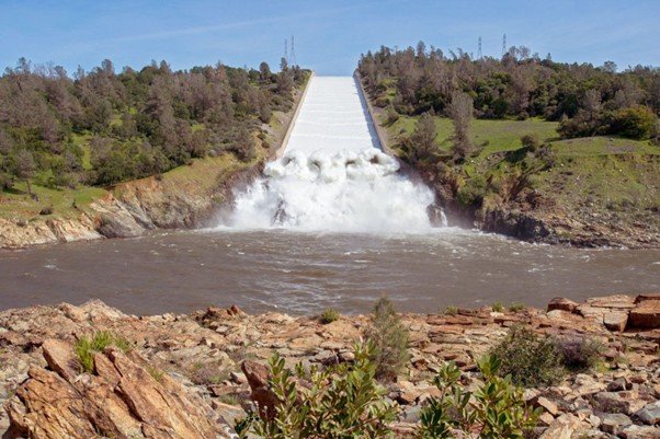 Water flowing down a large concrete spillway beside a reservoir wall.