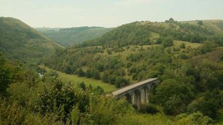 Large stone railway viaduct stretching across a green valley in open countryside.