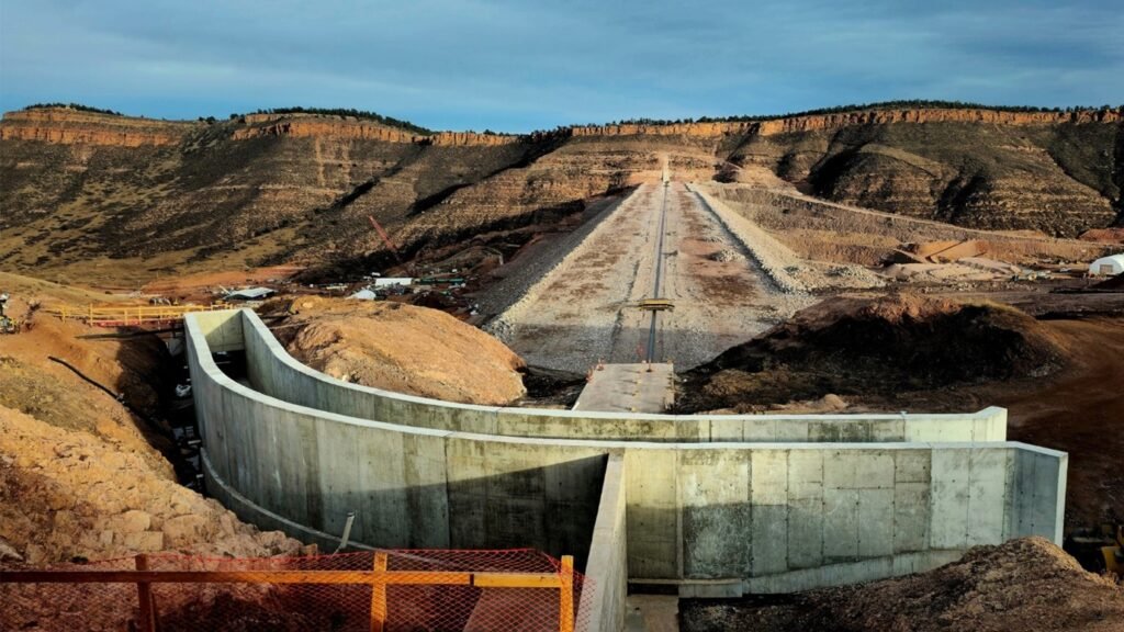 Large reservoir dam with concrete spillway descending down the slope.